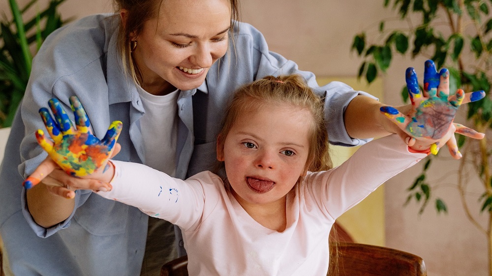 young-girl-with-down-syndrome-with-paint-on-palms-held-by-carer
